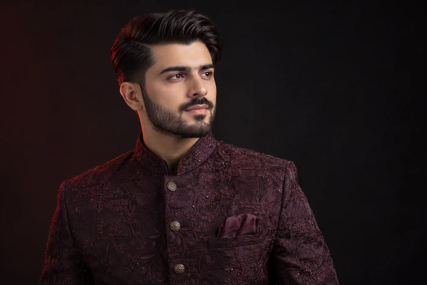 Side-parted wedding haircut with shorter sides and a shaped short beard above an aubergine jacket